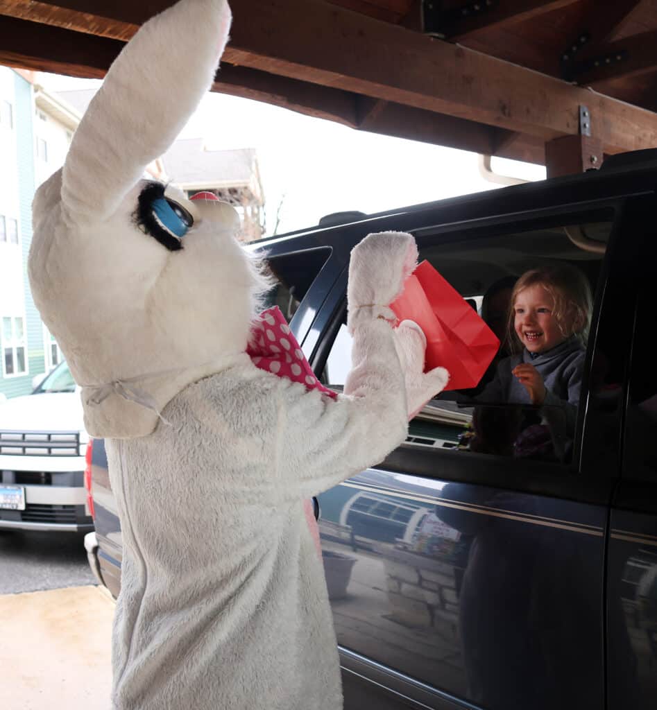 The Easter bunny hand a gift baskets to Woolgang Flores, 3, as families drive up to Timbers of Shorwood entrance Sunday, April 4, 2026, in Shorewood, Ill.